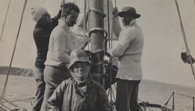 Молли Чайлдерс у руля яхты Asgard, пока ее муж с помощниками поднимает парус. 1914 г.